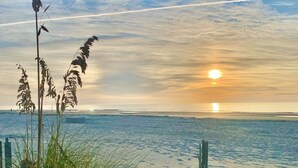 Una playa con una valla de madera, césped y una puesta de sol sobre el agua.