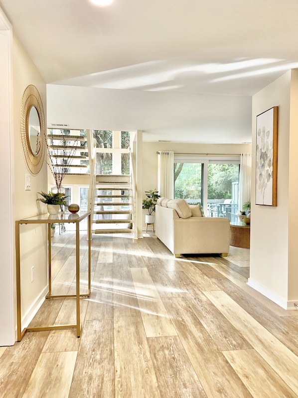 A spacious living area with a staircase, a sofa, and a large window offering a view of greenery.
