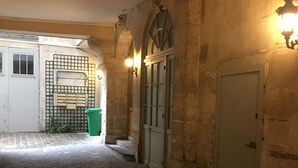 A narrow cobblestone corridor with stone walls, a green trash bin, and a door with a window. - Luxury Affordable Vacation Home in Paris, Marais (Paris)