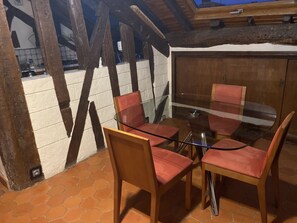 Un espace repas avec une table en verre et des chaises en bois, un sol carrelé et une vue sur l’extérieur.