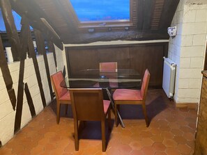 Un coin repas avec une table à plateau en verre et des chaises en bois, une vue par la fenêtre et un sol carrelé.