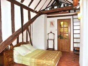 Une chambre avec un lit en bois, une chaise en bois, une porte avec des panneaux de verre et une échelle.