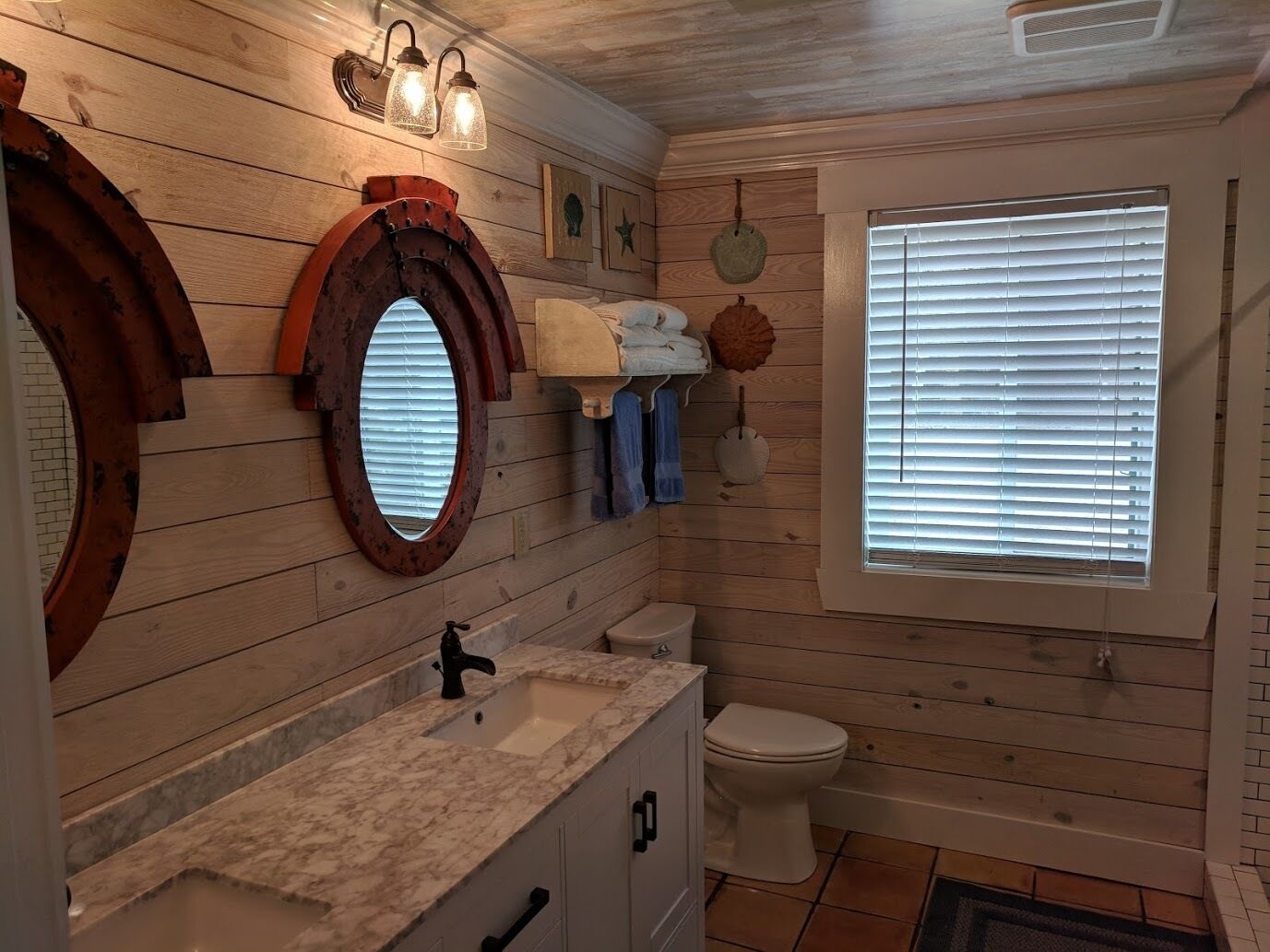 A bathroom with wooden walls, a marble sink, a toilet, and a window with blinds.