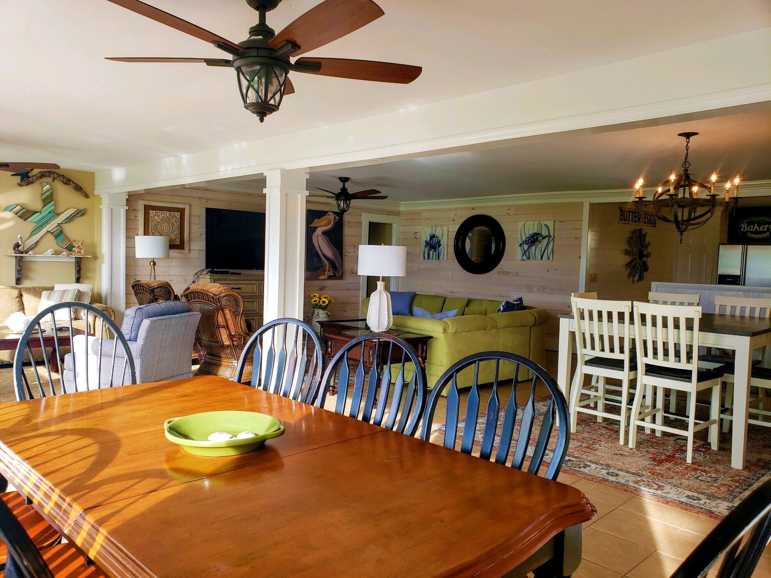 A dining area with a wooden table and chairs, a ceiling fan, and a dining table with a green bowl.