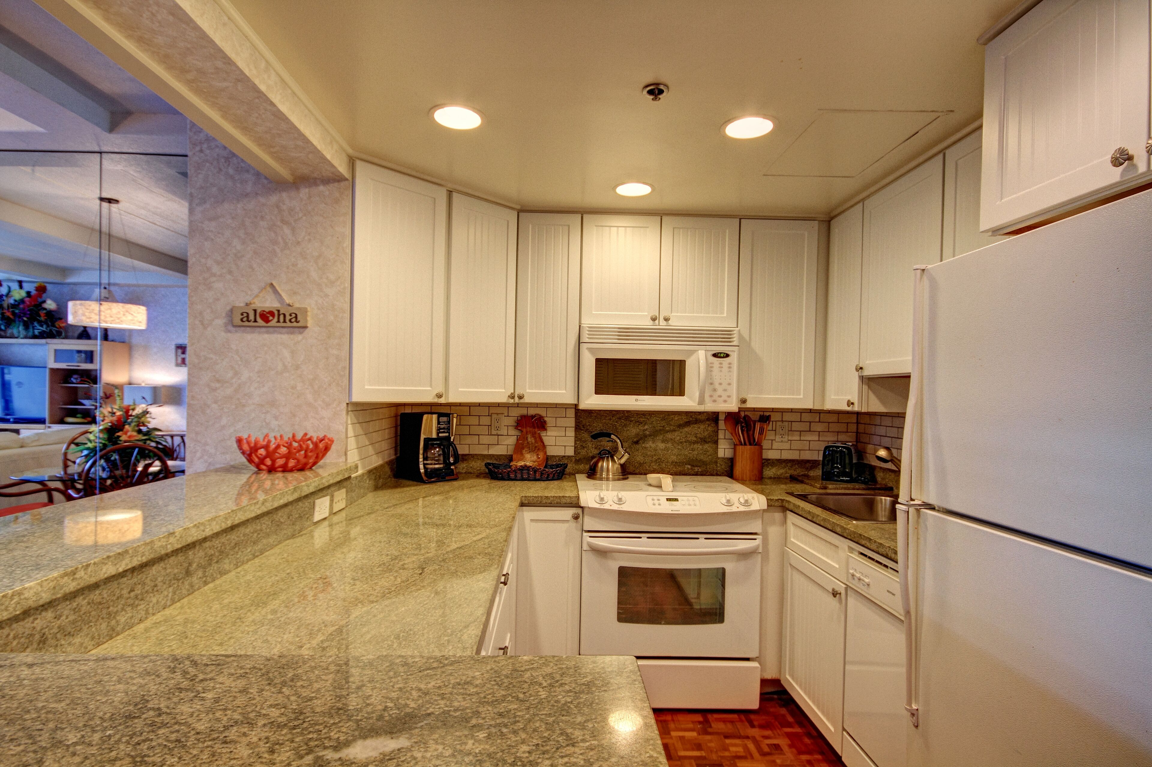 A modern kitchen with white cabinets, granite countertops, a stove, microwave, and a refrigerator.