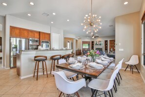 A spacious kitchen with modern appliances, a dining area with a long table set for six, and a cozy living room in the background.