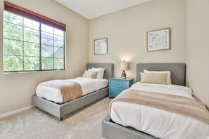 A bedroom with two beds, a nightstand, and a window with blinds.