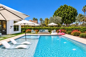 A swimming pool with lounge chairs, umbrellas, and a small inflatable unicorn float.