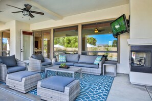 A sunlit patio with wicker furniture, a fireplace, and a TV mounted on the wall.