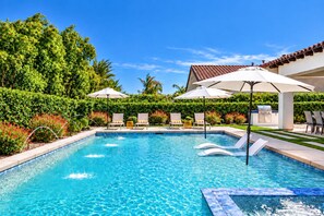 A swimming pool with lounge chairs and umbrellas, surrounded by greenery and a barbecue area. - Serenity in the Desert - Slow Down and Reconnect at Gentle Breeze (Indio)