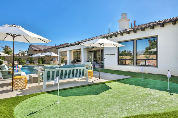 A backyard with a swimming pool, outdoor furniture, and umbrellas.