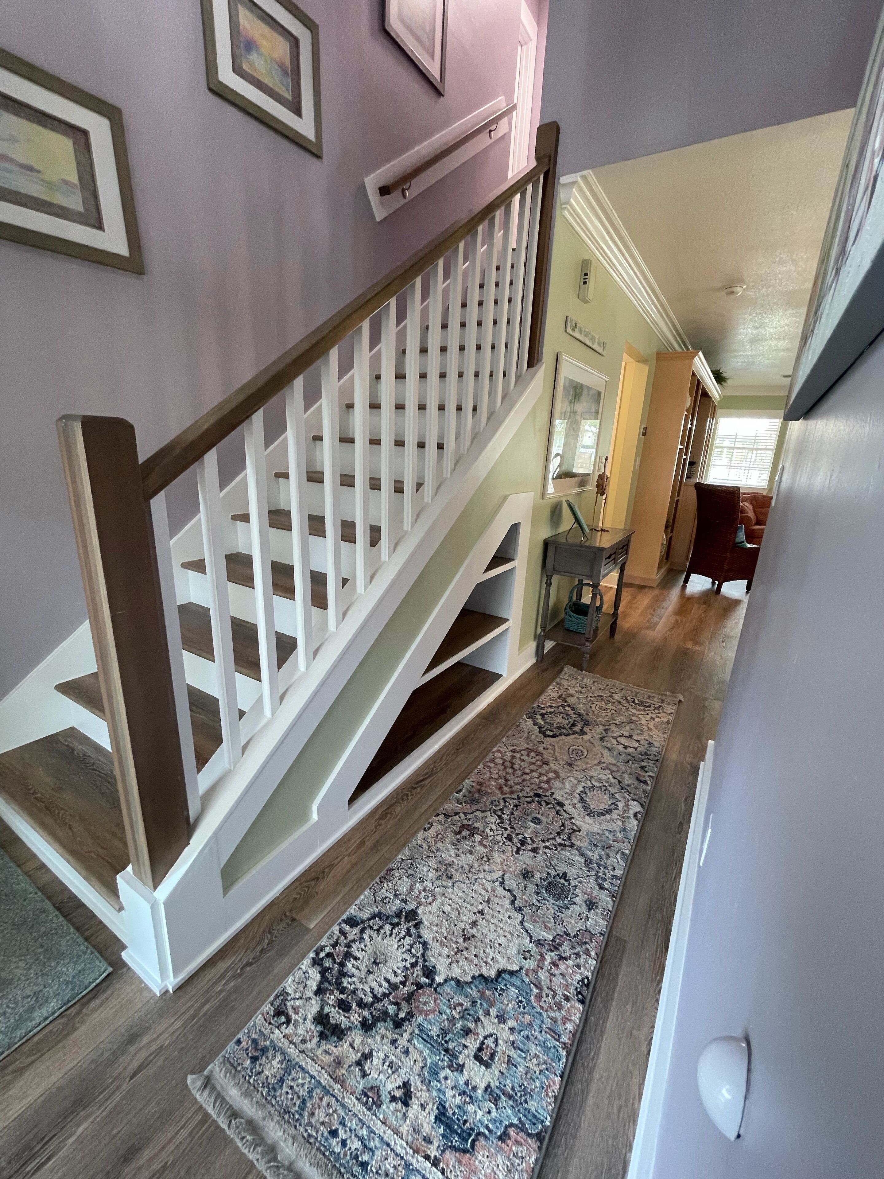 Una escalera con barandilla de madera y balaustres blancos, que conduce a un rellano con un tapete estampado.
