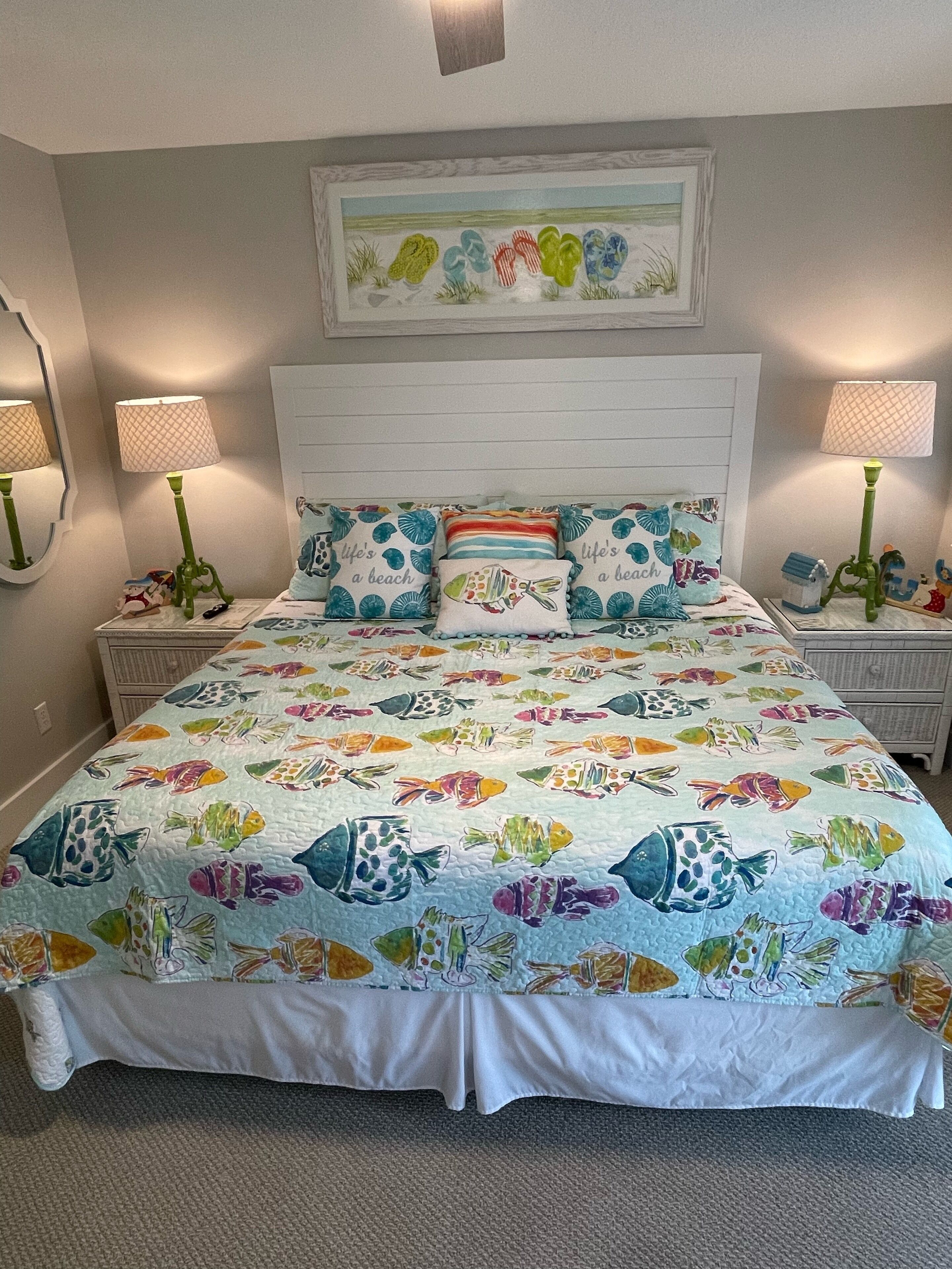 A bedroom with a bed featuring a colorful fish-patterned quilt, two nightstands with lamps, and a framed artwork above the bed.