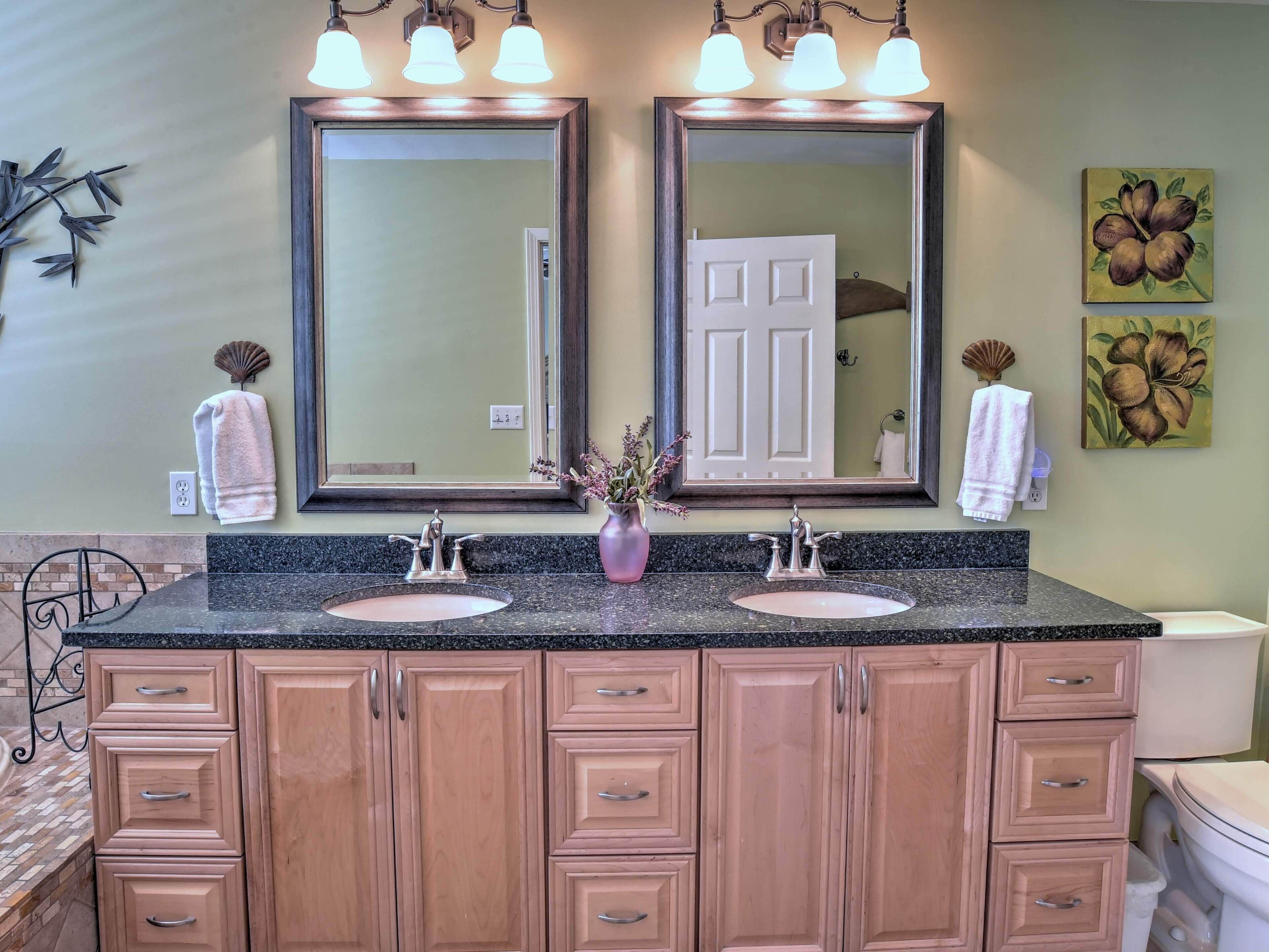 A bathroom with two sinks, a vanity with drawers, a mirror, and wall-mounted lights.