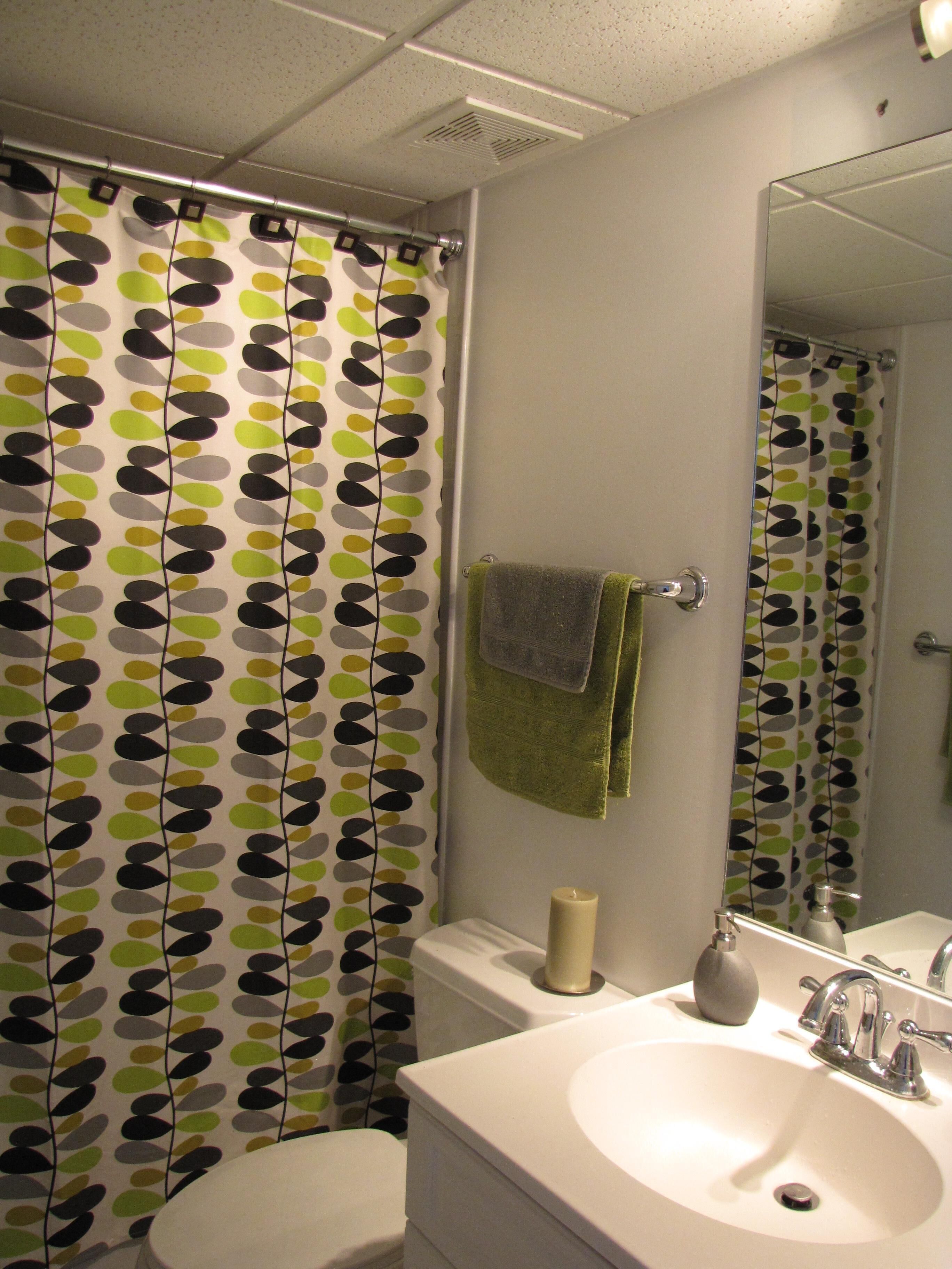 A bathroom with a shower curtain featuring a leaf pattern, a toilet, a sink with a mirror, and a towel hanging on the wall.