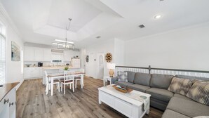 Un amplio espacio de estar con un sofá gris, una mesa de comedor con sillas y una cocina al fondo.