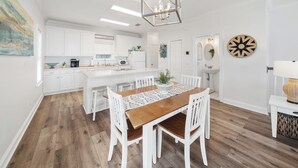Una cocina moderna con armarios blancos, una isla central y un comedor con mesa de madera y sillas blancas.