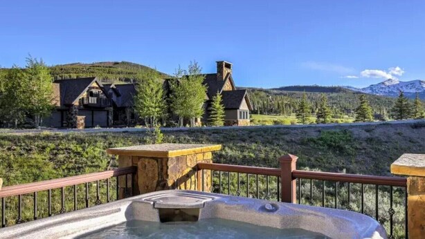 Een hottubgedeelte met stenen relingen, uitzicht op een lodge en een bergachtig landschap.