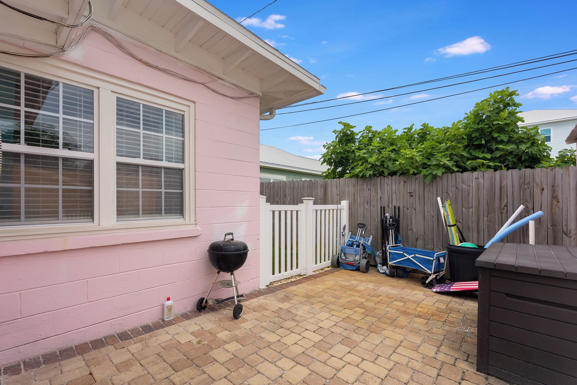 A backyard with a pink house, a wooden fence, a grill, and a small shed.