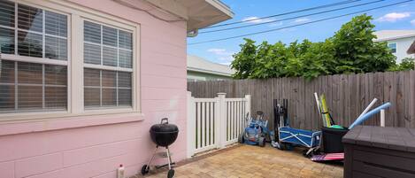 A backyard with a pink house, a wooden fence, a grill, and a small shed.