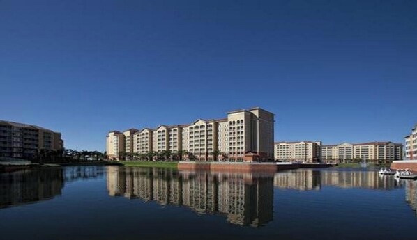 Et hotel med flere bygninger, en rolig sø foran og klare himmel.