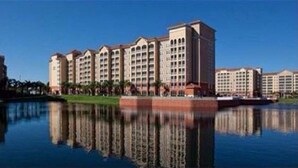 Un hotel con varias edificaciones, un cuerpo de agua reflectante al frente y un cielo despejado.
