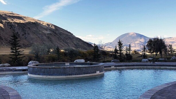 En swimmingpool med en cirkelformet stenskulptur i midten, omgivet af en belagt terrasse.