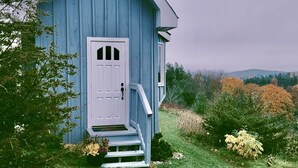 A small, single-story blue house with a white door and steps leading up to it. - Exquisite Accommodations Farmhouse with over 100 acres (Castleton)