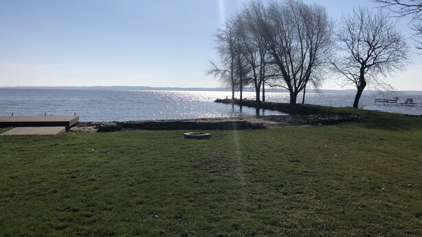 A grassy area with a body of water, trees, and a distant view of land. - Lake Winnebago Waterfront Cottage W/Hot Tub
[2 King; 1 Queen] (Fond du Lac)