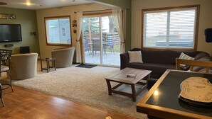 A living room with a sofa, a coffee table, a TV, and a dining table. - Lake Winnebago Waterfront Cottage W/Hot Tub
[2 King; 1 Queen] (Fond du Lac)