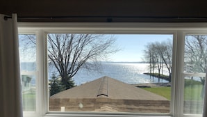 A window with a view of a lake and a grassy area with trees. - Lake Winnebago Waterfront Cottage W/Hot Tub
[2 King; 1 Queen] (Fond du Lac)