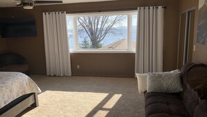 A bedroom with a bed, a couch, a window with curtains, a ceiling fan, and a view of trees and a building outside. - Lake Winnebago Waterfront Cottage W/Hot Tub
[2 King; 1 Queen] (Fond du Lac)