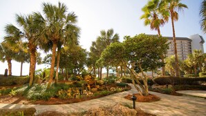 Un jardín ajardinado con palmeras, un sendero pavimentado y un edificio al fondo.