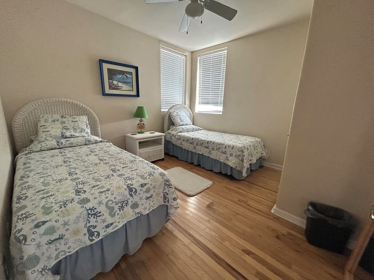 A bedroom with two single beds, a nightstand, a lamp, and a ceiling fan.