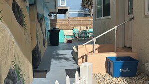 A covered outdoor area with a white fence, a blue recycling bin, and a patio with chairs and a table. - Beachfront Spanish Style Landmark 3 Bedroom 2 bath House (Flagler Beach)
