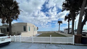 A residential property with a white picket fence, a paved driveway, and a house with a light-colored exterior. - Beachfront Spanish Style Landmark 3 Bedroom 2 bath House (Flagler Beach)