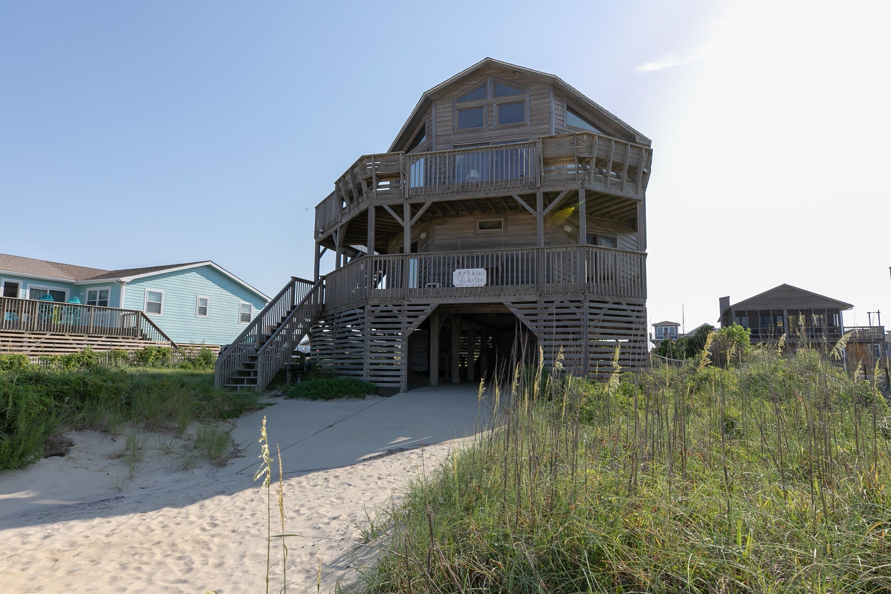 Una casa sulla spiaggia in legno con un balcone, una scala e un cartello.