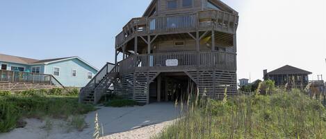 Una casa sulla spiaggia in legno con un balcone, una scala e un cartello.