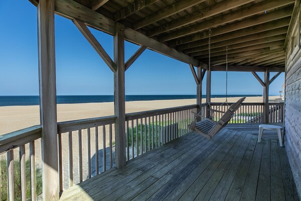 Une terrasse en bois avec un hamac et un banc donnant sur une plage.