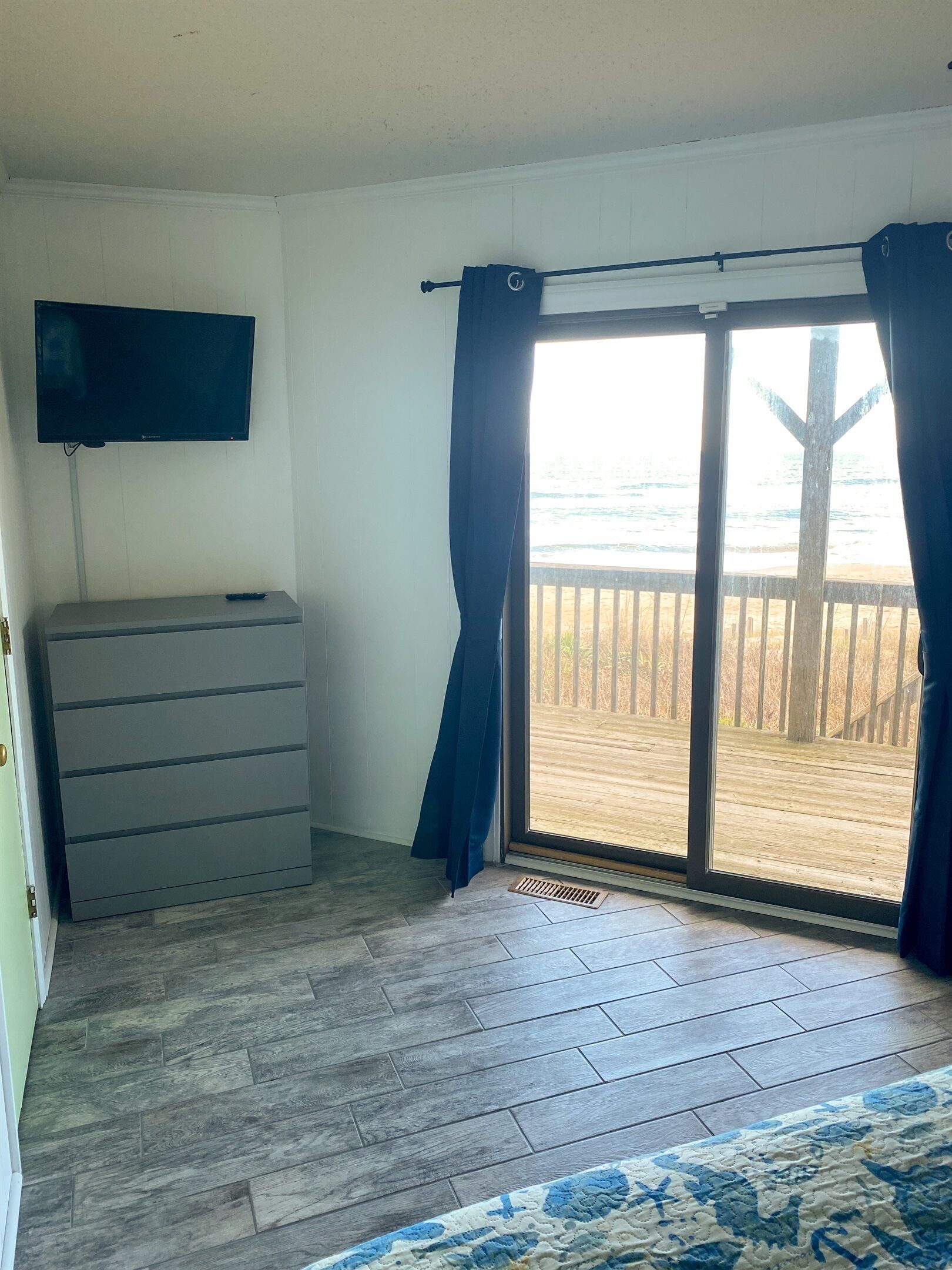 Een kamer met een grijze dressoir, een wandtelevisie en een grote schuifpui naar een houten terras.