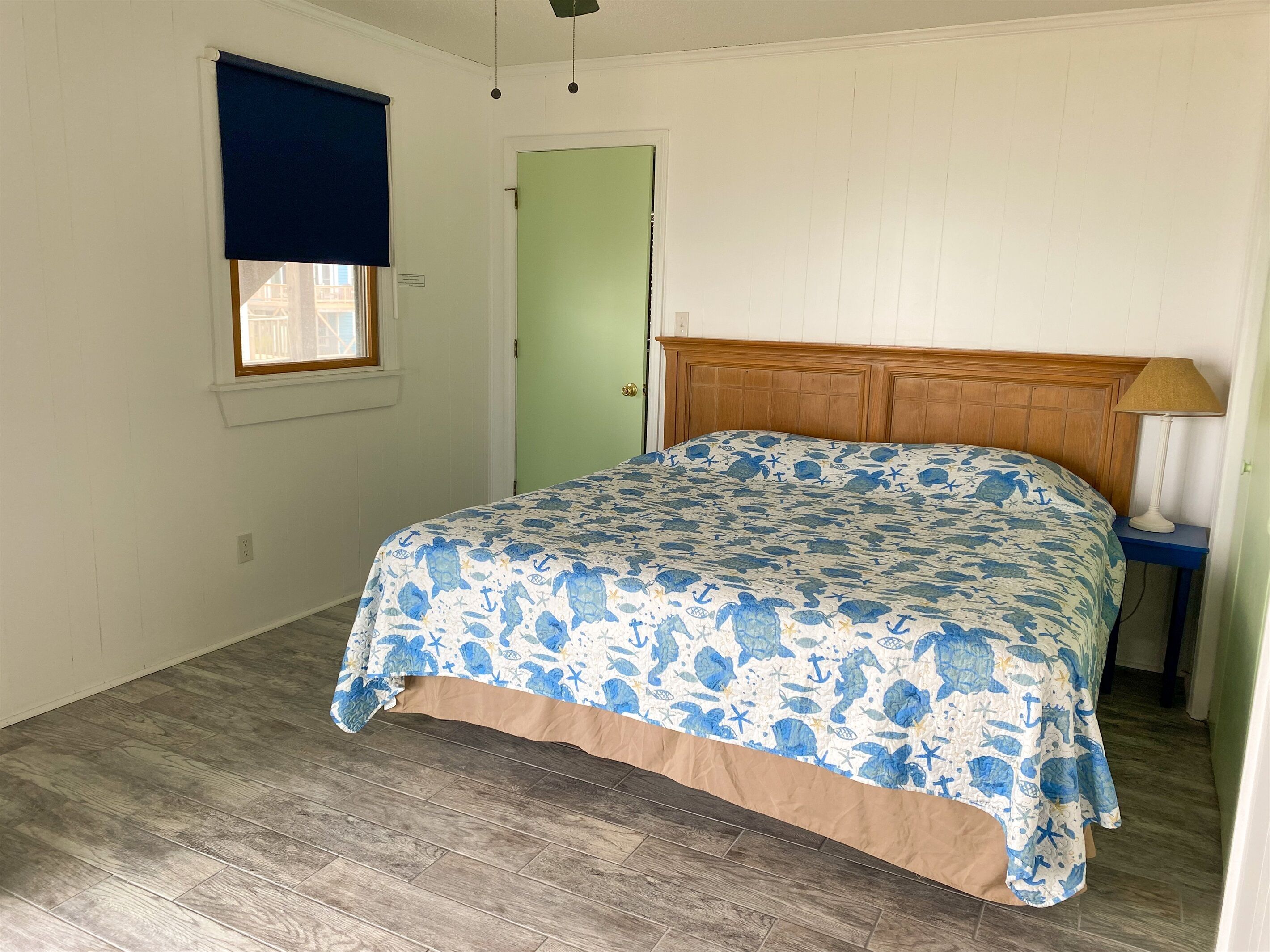 Une chambre à coucher comprenant un lit, une table de chevet, une lampe, une fenêtre avec un store et une porte.