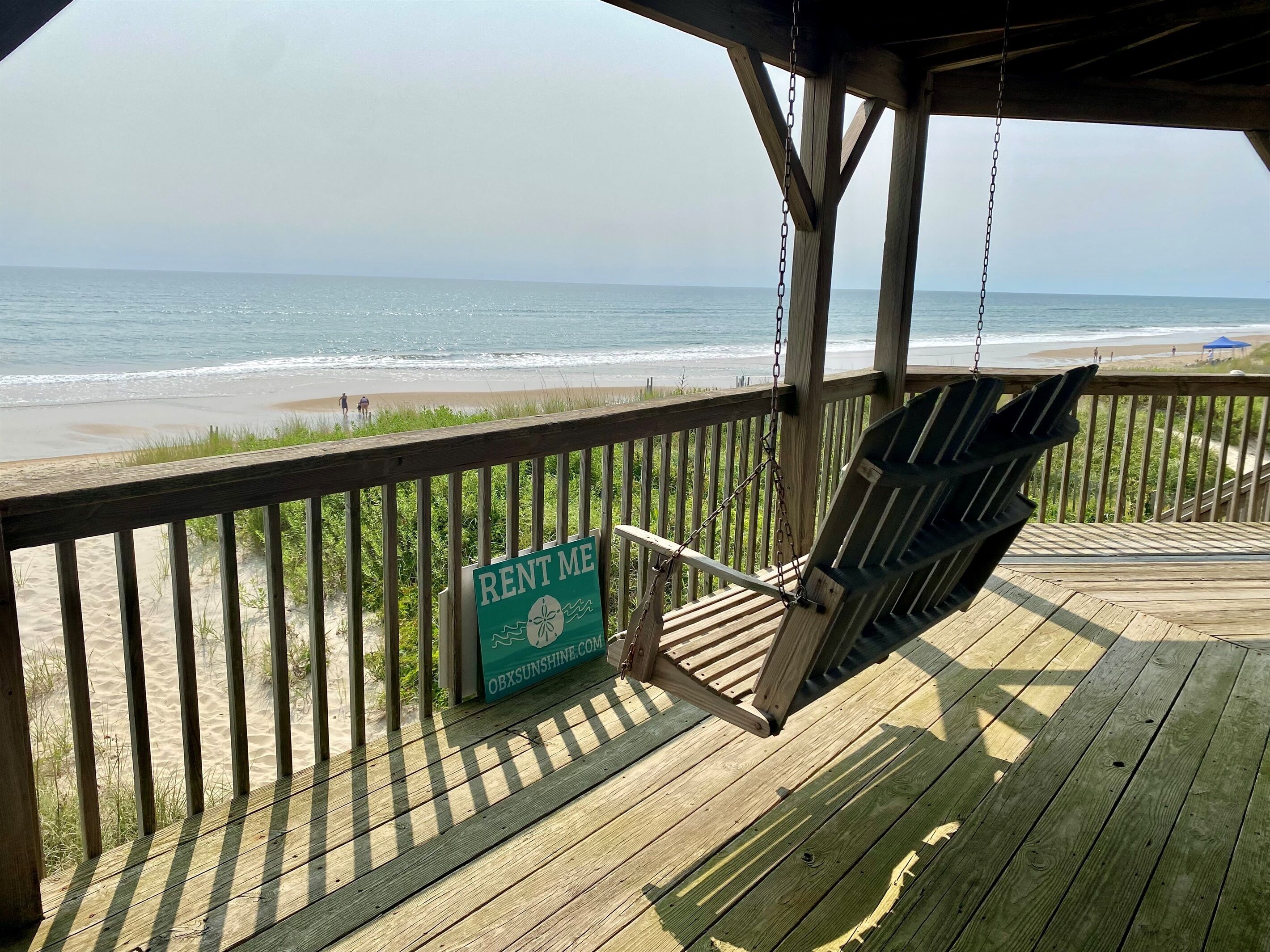 Una terraza de madera con un letrero que dice 'RENT ME', con vista a una playa.