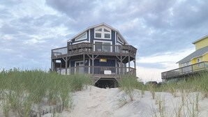 Une maison de plage à deux étages, dotée d’une terrasse en bois et de plusieurs balcons.