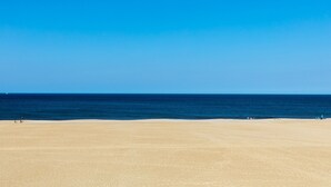 Une vaste plage de sable fin, sous un ciel bleu dégagé et une mer calme.