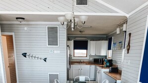 Une cuisine moderne avec des meubles blancs, un plan de travail en bois et un coin repas comprenant une table en verre et des chaises blanches.