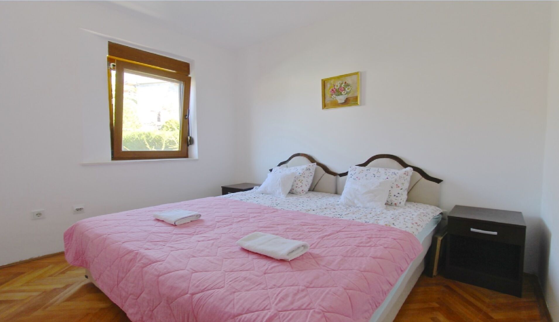 Un dormitorio con cama, mesita de noche, ventana y un cuadro en la pared.