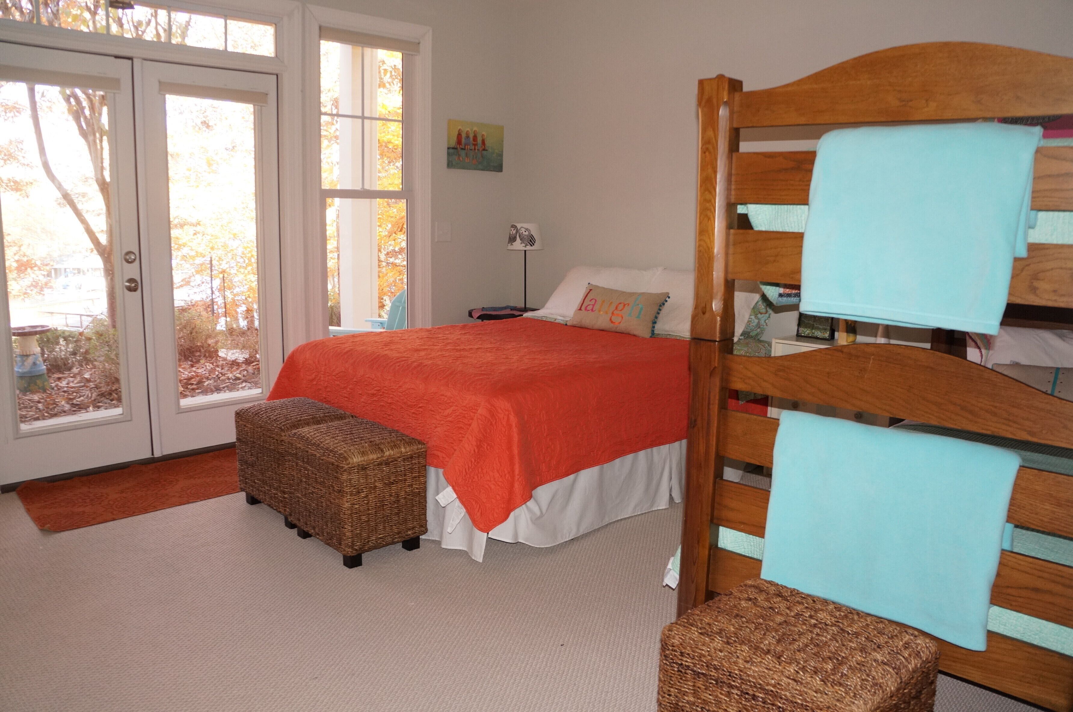 Een slaapkamer met een bed, een houten hoofdbord, een nachtkastje, een lamp en een raam met uitzicht op bomen.