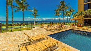 A poolside area with lounge chairs, palm trees, and a view of the ocean.