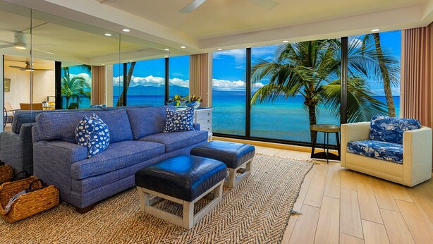 A modern living room with a large window offering a view of the ocean and palm trees.