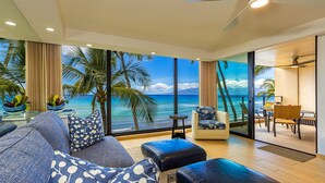 A modern living room with a large window overlooking a beach, a sofa, a chair, and a dining area.